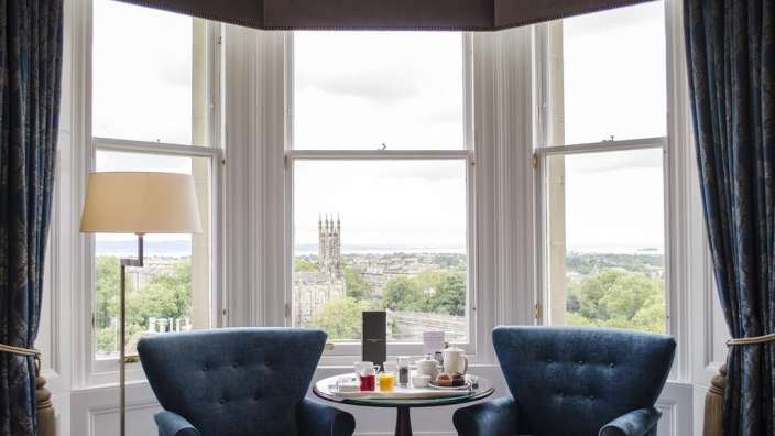 Zwei blaue Stühle sitzen an einem Tisch vor einem großen Fenster