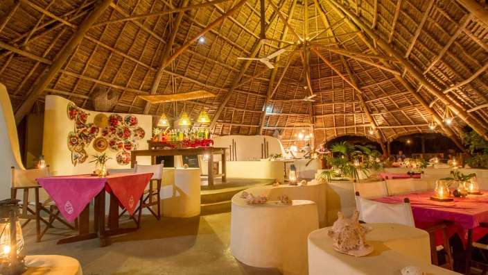 Ein großer Raum mit einem Strohdach und Tischen und Stühlen