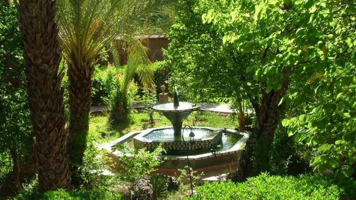 Ein Brunnen in einem Garten umgeben von Bäumen und Palmen