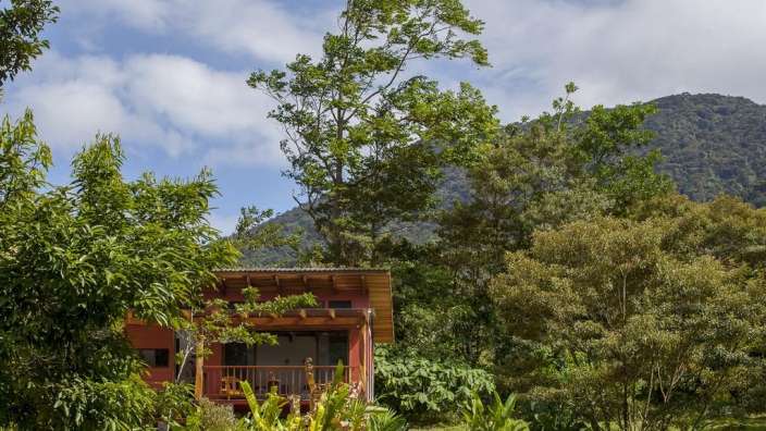 Ein kleines rotes Haus mit einer Veranda umgeben von Bäumen und Bergen