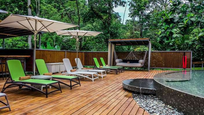 Ein Holzdeck mit grünen Stühlen und weißen Regenschirmen