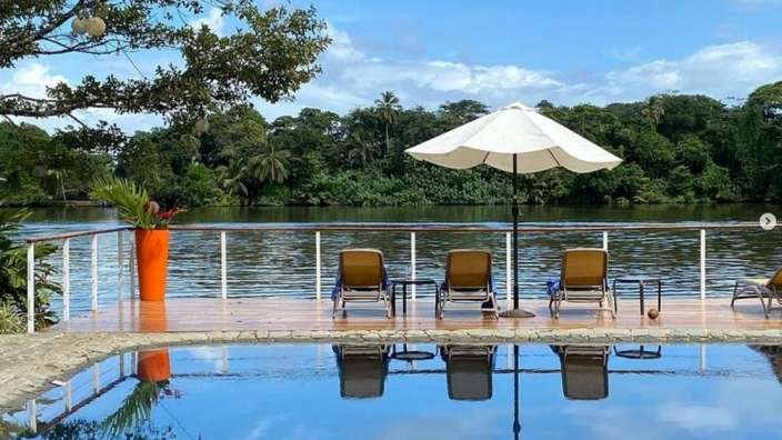 Ein Pool mit Stühlen und einem weißen Regenschirm neben einem Fluss