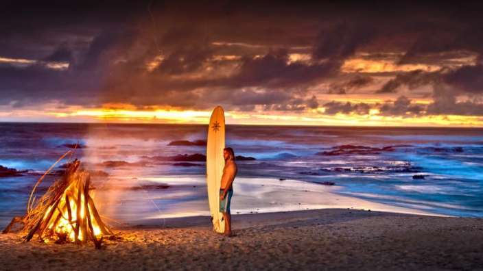 Ein Mann steht neben einem Surfbrett am Strand