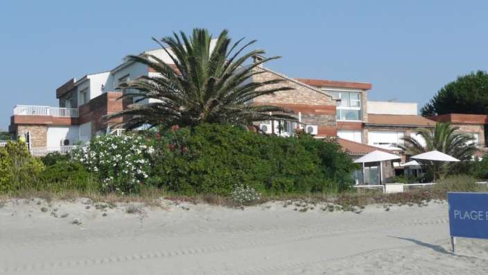 Ein blaues Schild steht auf einem Sandstrand in der Nähe eines großen Hauses
