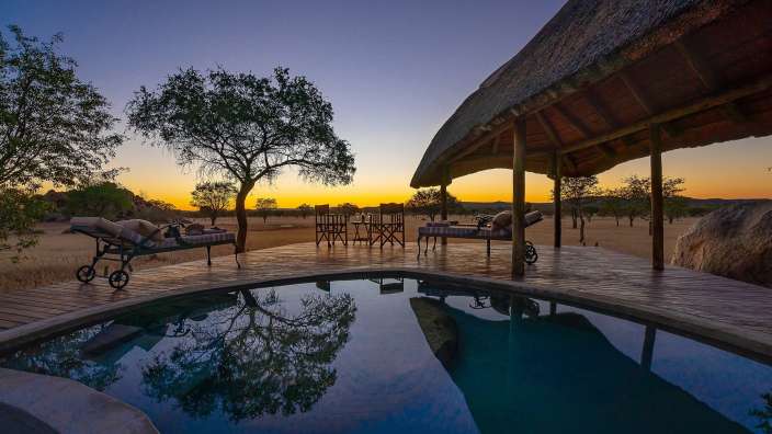 Ein schwimmbad mit einem strohdach und einem sonnenuntergang im hintergrund