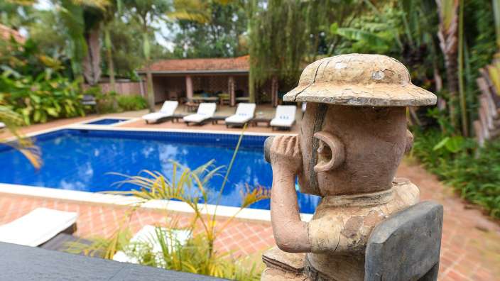 Eine Statue eines Mannes sitzt vor einem Swimmingpool