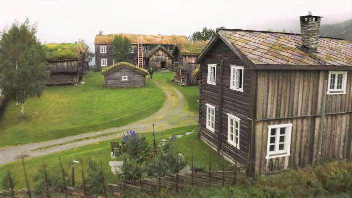 Ein kleines Holzhaus mit weißen Fenstern steht inmitten eines grünen Feldes