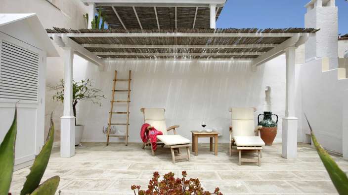 Liegestühle stehen unter einem weißen Pergoladach