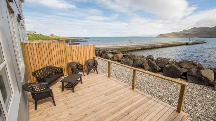 Ein Holzdeck mit Möbeln und einem Zaun mit Blick auf das Meer