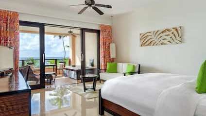 Ein Hotelzimmer mit einem Kingsize-Bett, einem Couchtisch, einem Fernseher und einem Deckenventilator .