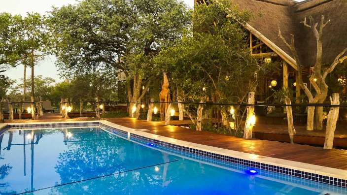 Ein großer Swimmingpool mit einem Holzdeck umgeben von Bäumen