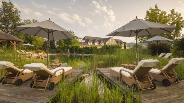 Liegestühle und Sonnenschirme stehen neben einem Teich