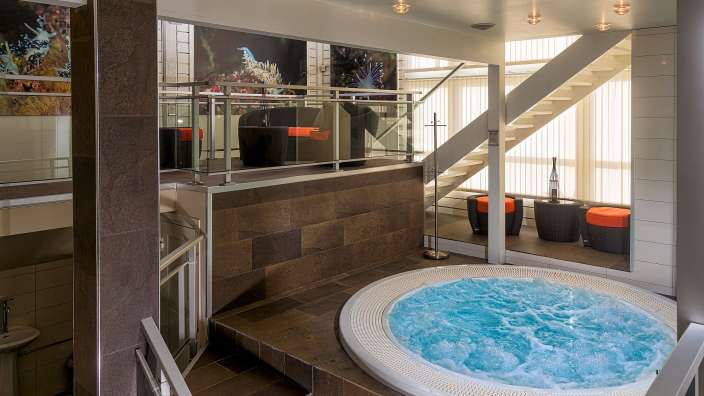 Ein Whirlpool mit blauem Wasser in einem Badezimmer neben einer Treppe