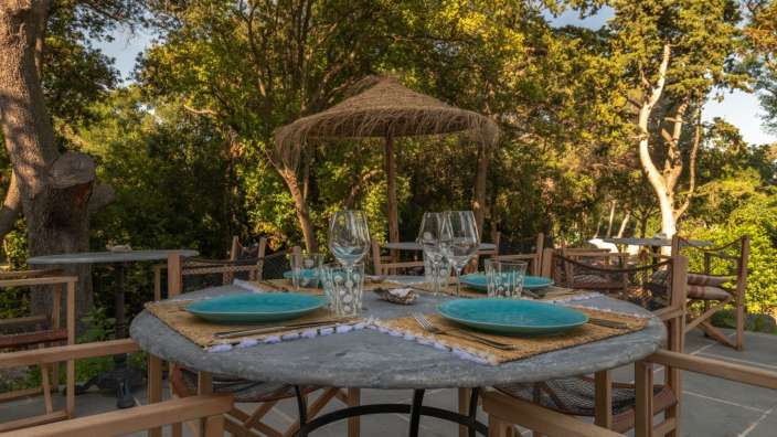 Ein Tisch mit blauen Tellern und Gläsern unter einem Strohschirm