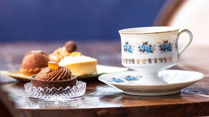 Eine weiße Tasse mit blauen Blumen darauf sitzt auf einem Tisch neben einem kleinen Kuchen