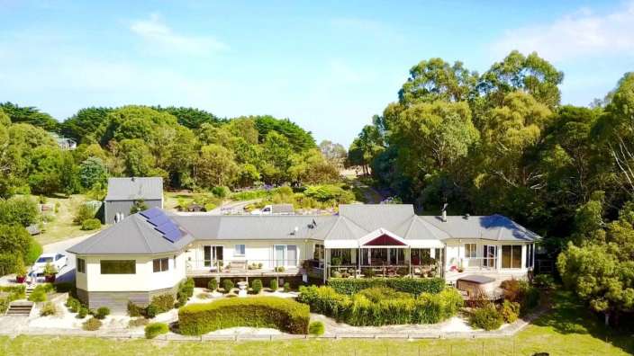 Ein großes weißes Haus mit einem schwarzen Dach steht inmitten von Bäumen