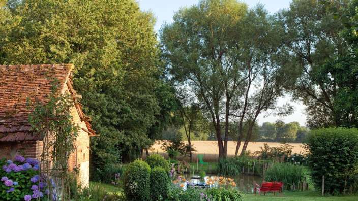 Eine rote Bank sitzt in einem Garten neben einem Teich