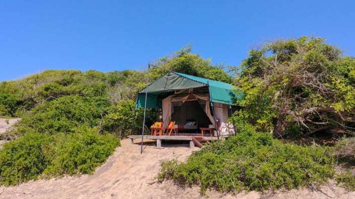 Ein Zelt mit einem grünen Zeltdach sitzt auf einem sandigen Hügel