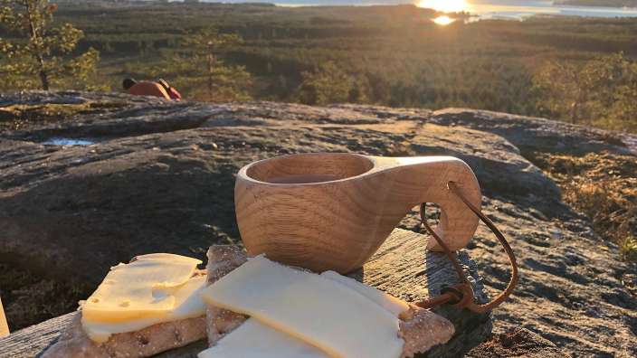 Eine Tasse Kaffee steht auf einem Felsen neben einem Stück Brot und Käse