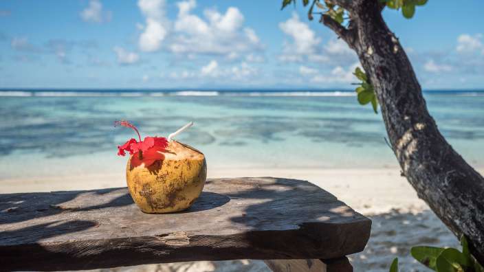 Eine Kokosnuss mit einer Blume darin sitzt auf einem Holztisch am Strand