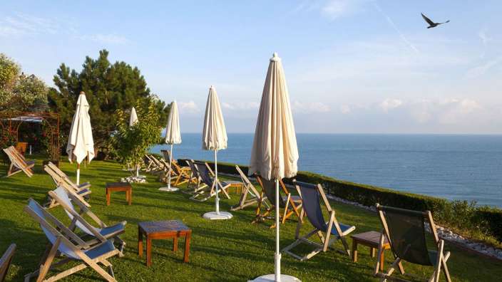 Liegestühle und Sonnenschirme auf einer Wiese mit Blick auf das Meer