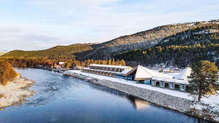 Ein Gebäude neben einem Fluss mit Bergen im Hintergrund