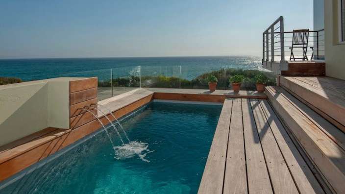 Ein kleiner Pool mit einem Wasserfall auf einem Holzdeck mit Blick auf den Ozean