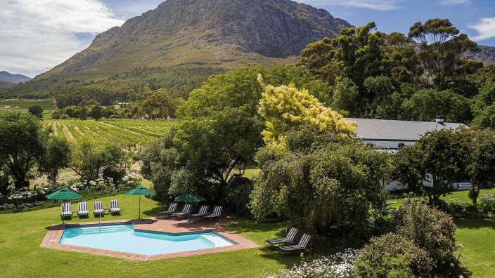 Ein Pool mit Stühlen und Sonnenschirmen in einem Garten mit einem Berg im Hintergrund