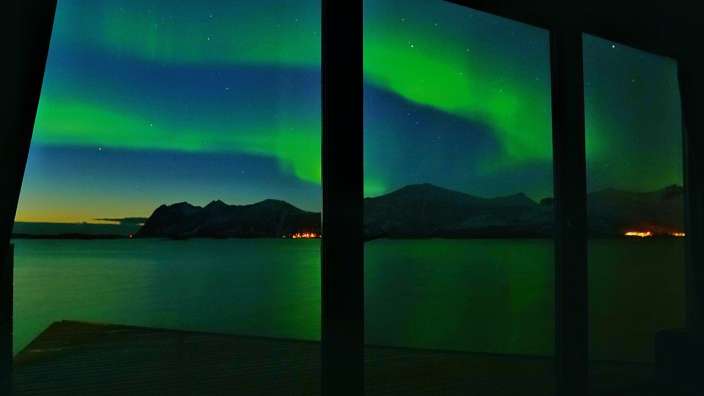 Das Nordlicht scheint aus einem Fenster über einen See