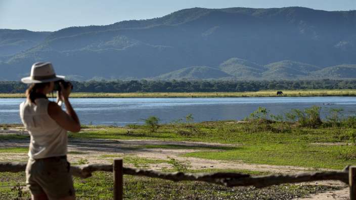 Eine Frau fotografiert einen See mit Bergen im Hintergrund