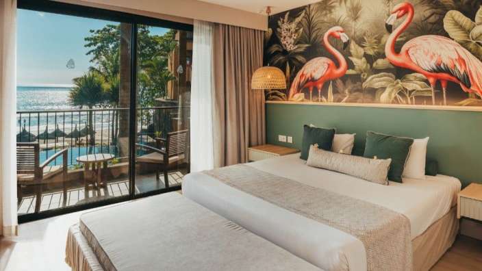 Ein luxuriöses Schlafzimmer mit Blick auf das Meer und den Strand, geschmückt mit Flamingos und tropischen Pflanzen an der Wand.