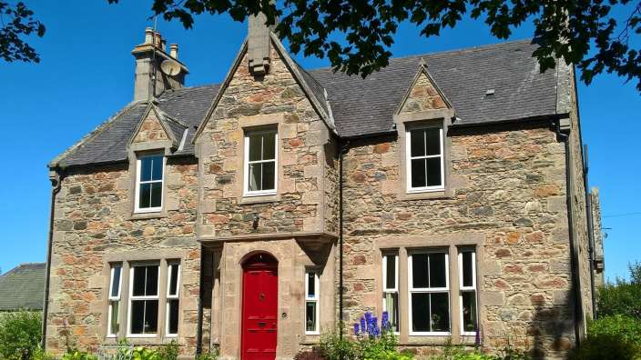 Ein großes Steinhaus mit einer roten Tür und weißen Fenstern