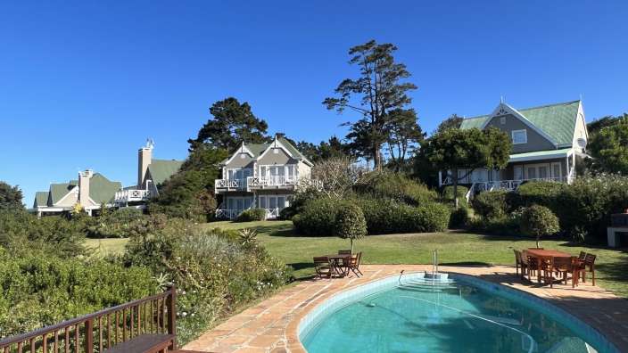 Ein großes weißes Haus mit einem grünen Dach steht neben einem großen Swimmingpool