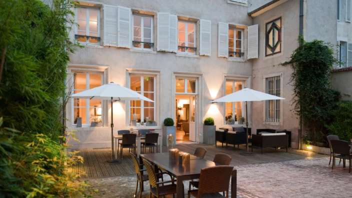 Eine Terrasse mit Tisch und Stühlen vor einem Gebäude mit weißen Fensterläden
