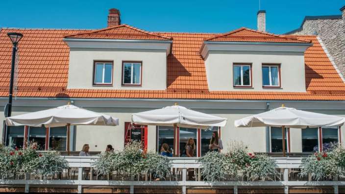 Eine Gruppe von Menschen sitzt vor einem Gebäude mit weißen Sonnenschirmen