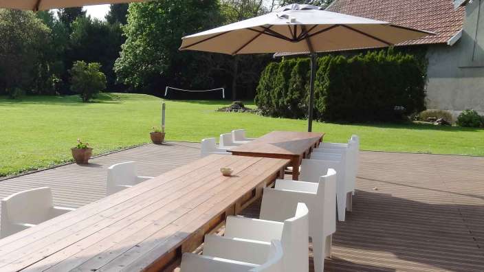 Ein langer Holztisch mit weißen Stühlen und Regenschirmen