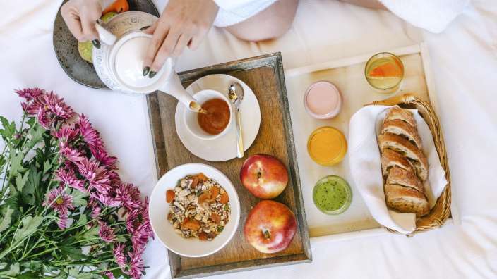 Eine Frau sitzt auf einem Bett mit einem Tablett voller Essen