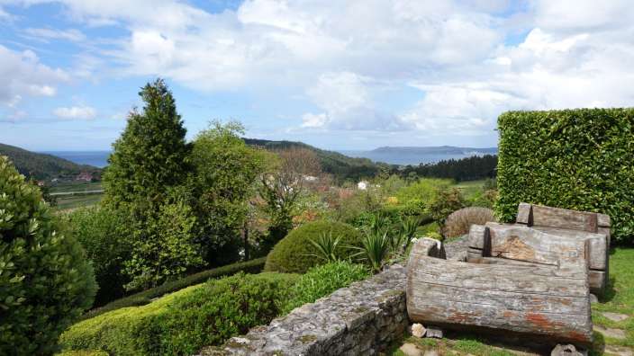 Ein hölzerner Stuhl steht in einem Garten mit Blick auf den Ozean