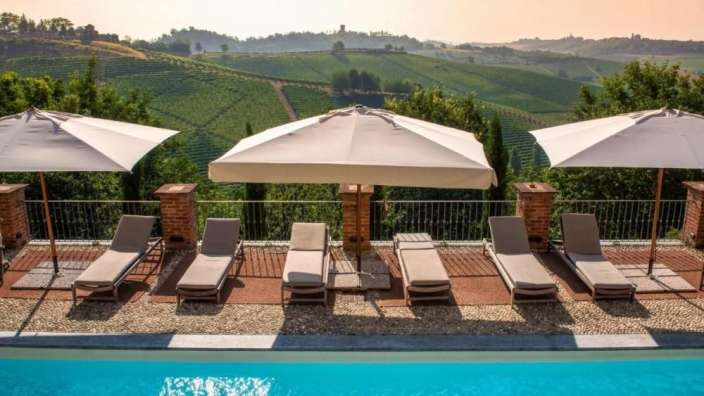 Liegestühle und Sonnenschirme um einen Pool mit Weinbergen im Hintergrund