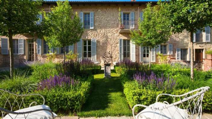 Ein Garten mit Stühlen und Bäumen vor einem großen Steingebäude