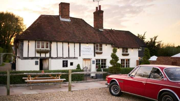 Ein rotes Auto steht vor einem weißen Gebäude mit der Aufschrift " die drei Schornsteine "