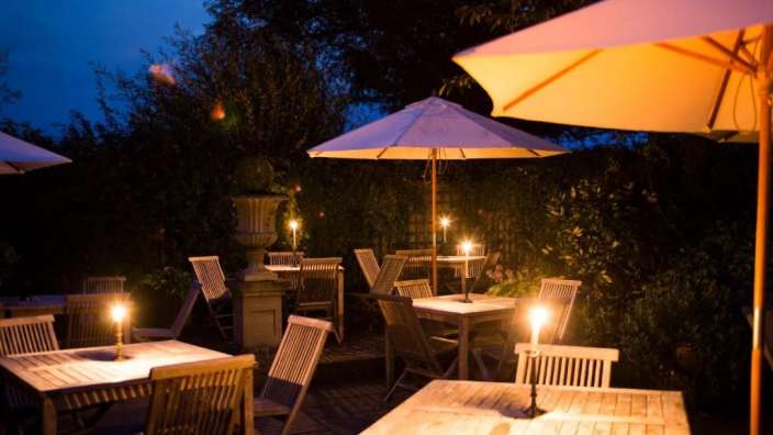 Tische und Stühle in einem Garten mit Kerzen und Regenschirmen