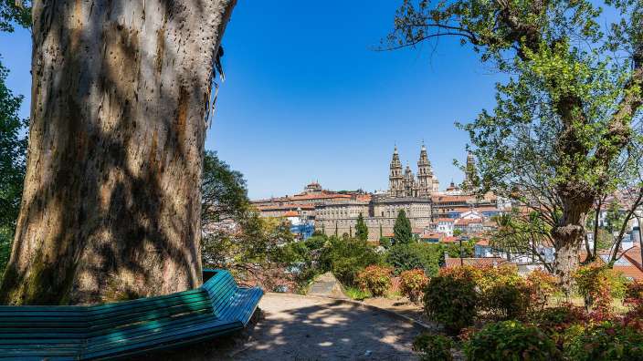 Ziel des Jakobswegs: Santiago di Compostela Eine Bank sitzt unter einem Baum mit einer Stadt im Hintergrund