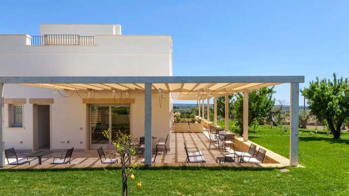 Ein weißes Haus mit einem Holzdeck und Stühlen darauf