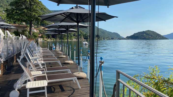 Liegestühle und Sonnenschirme auf einem Holzdeck mit Blick auf einen See