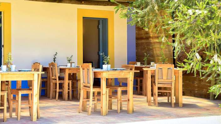 Eine Terrasse mit Holztischen und Stühlen vor einem gelben und blauen Gebäude