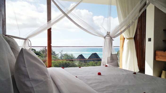 Ein Schlafzimmer mit einem Himmelbett und einem Balkon mit Blick auf den Ozean