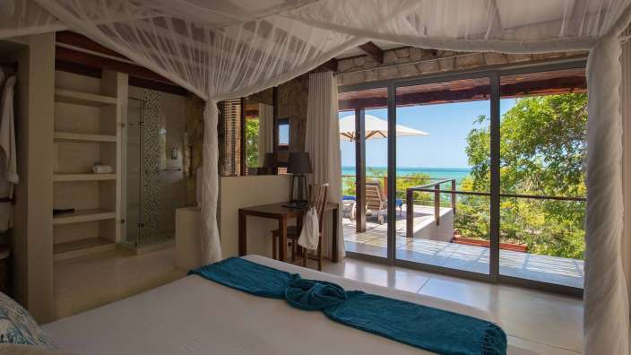 Ein Schlafzimmer mit einem Himmelbett und einer Schiebetür mit Blick auf den Ozean