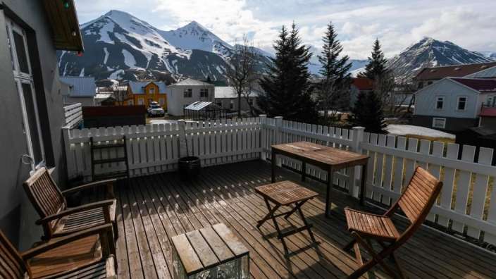 Eine Terrasse mit einem Tisch und Stühlen und einem weißen Zaun mit Bergen im Hintergrund