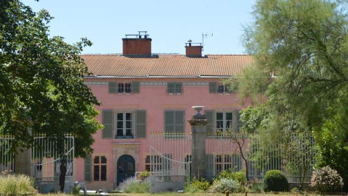 Ein rosafarbenes Haus mit grünen Fensterläden und einem roten Dach